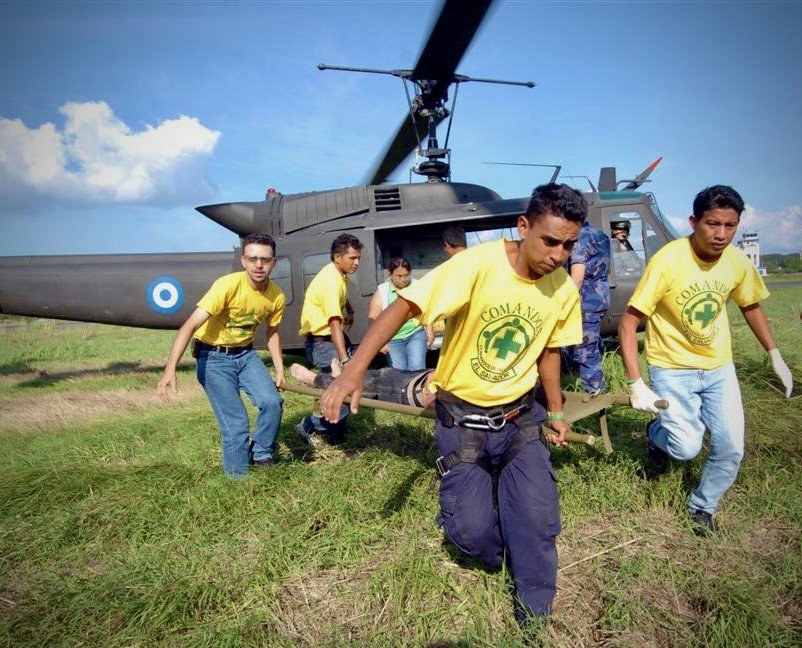 Voluntarios de Comandos de Salvamento trasladan a una persona junto a un helicóptero Huey